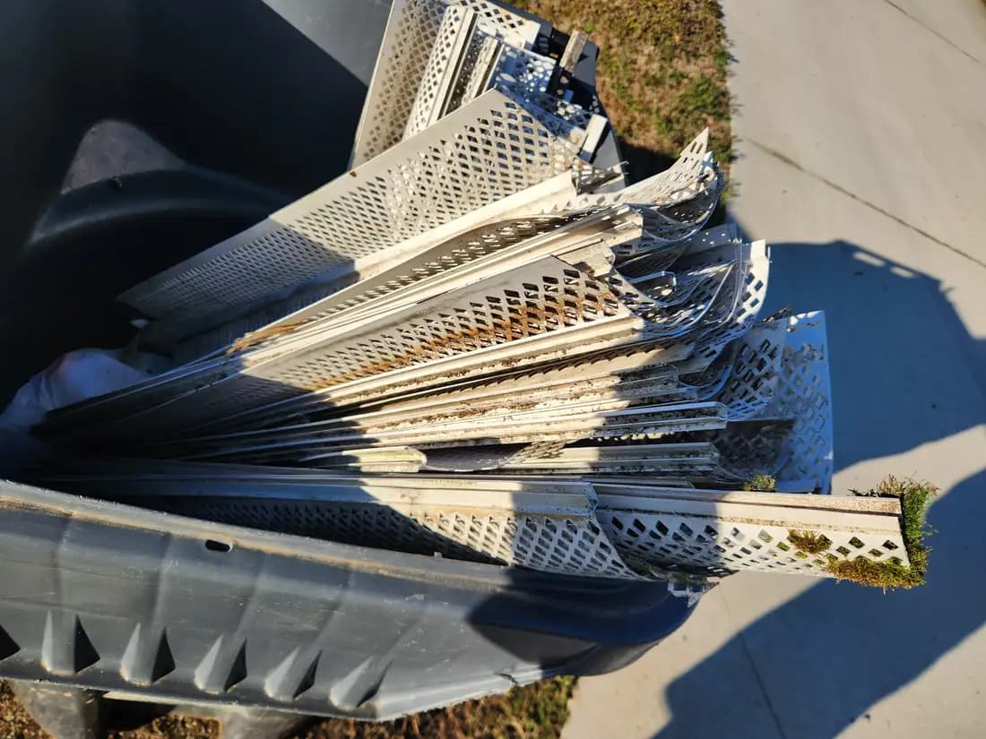 Pile of aged white plastic gutter guards pulled off an Alamance County NC home, warped panels with moss growth and brittle perforated edges from years of weather