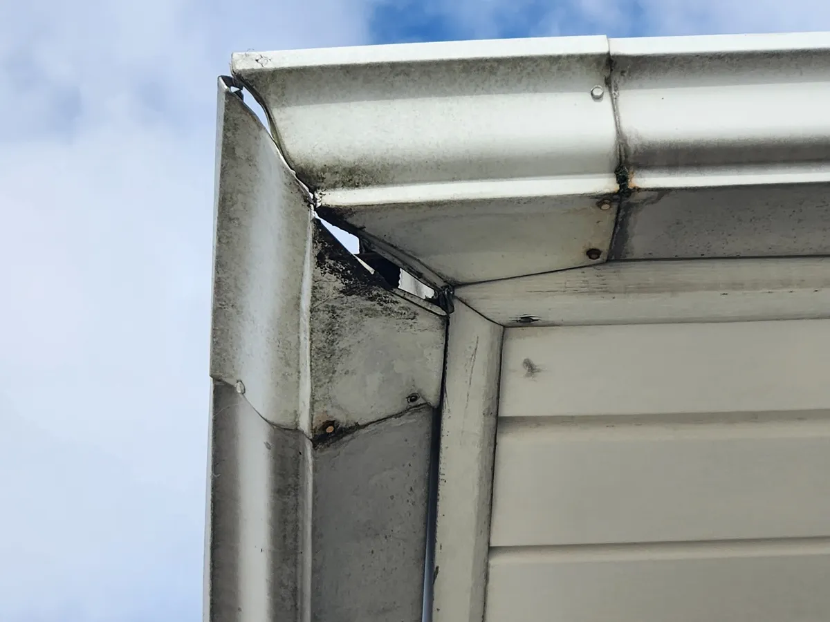 Close-up of gutter interior showing spike and ferrule attachment points with visible debris and water staining