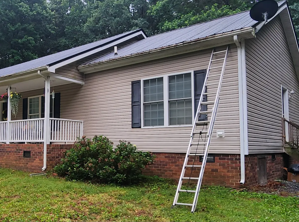 Extension ladder leaning against the siding of a single-story metal-roof home, set up for gutter cleaning in Alamance County NC